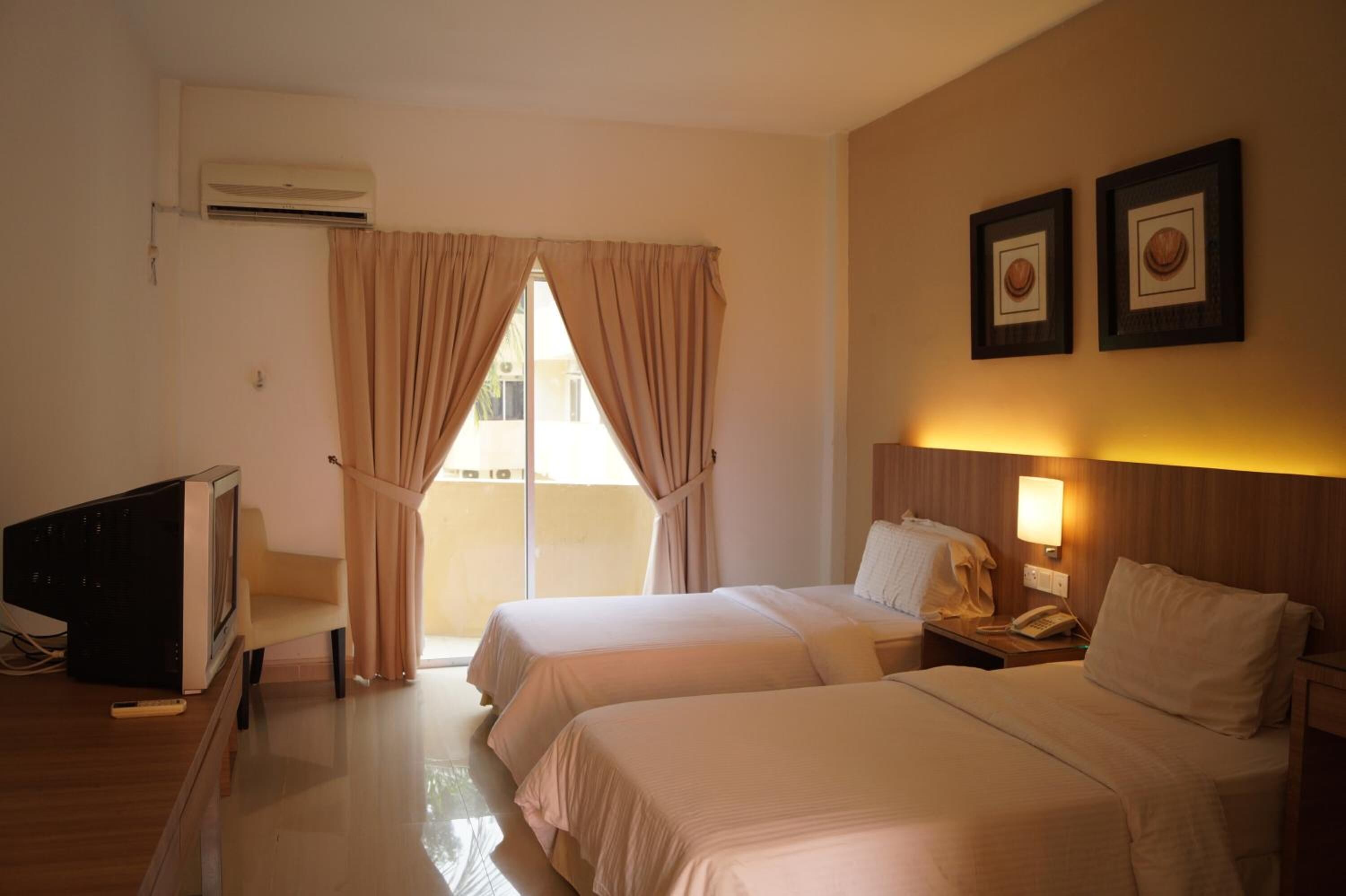 A hotel room with two beds, a TV, a desk, and a balcony with curtains.