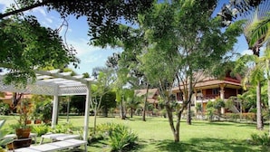 Un jardin agrémenté d’une pergola, de palmiers et d’un bâtiment au toit rouge.