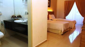 A hotel room with a bathroom featuring a sink, toilet, and shower. There are two beds with white bedding and a window with curtains.