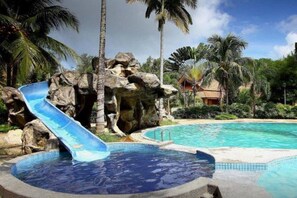 Un área de piscina con tobogán de agua, palmeras y paisaje rocoso.