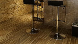 A bar area with two Apple monitors on a wooden shelf, two bar stools, and a stone wall. - The Haven by JetQuay (Singapore)
