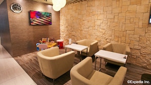 A modern interior with stone walls, a clock, a TV, and seating arrangements. - The Haven by JetQuay (Singapore)