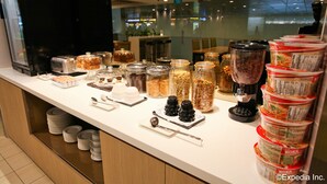 A buffet counter with various food items, including jars of nuts, a coffee machine, and stacked containers of food. - The Haven by JetQuay (Singapore)