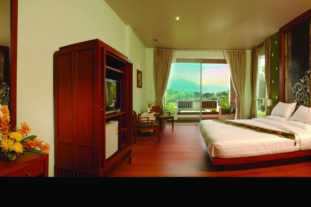 Una habitación de hotel con una cama grande, un escritorio con computadora, un televisor y vistas al exterior.