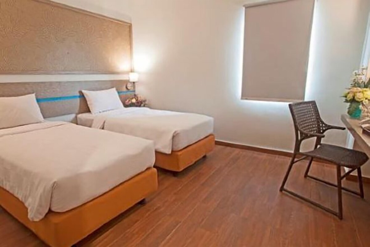Una habitación de hotel con dos camas individuales, piso de madera, un escritorio con silla y ventana con vista.