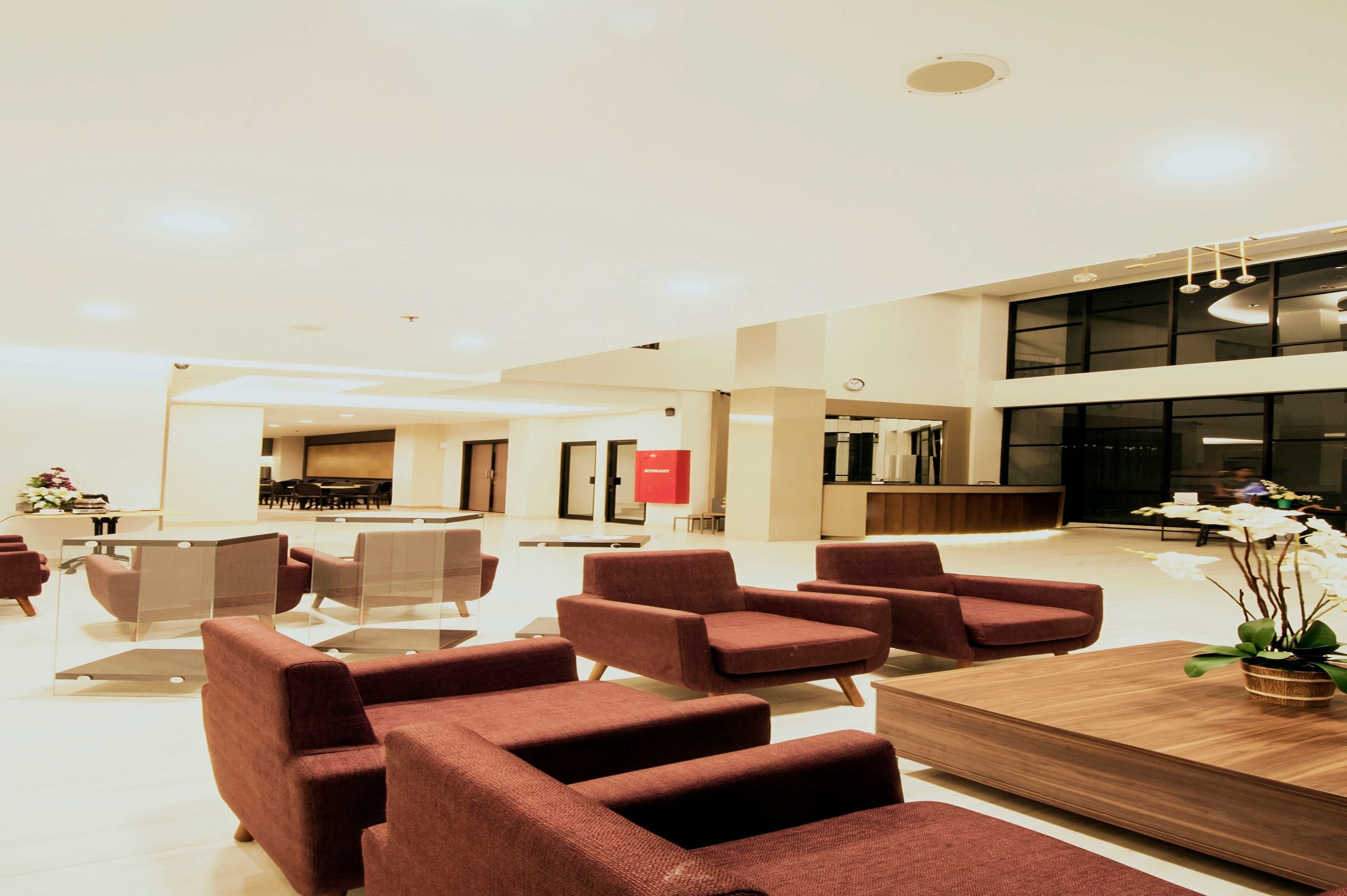 Een moderne lobby met rode bekleden stoelen, een houten receptiebalie en een groot raam.