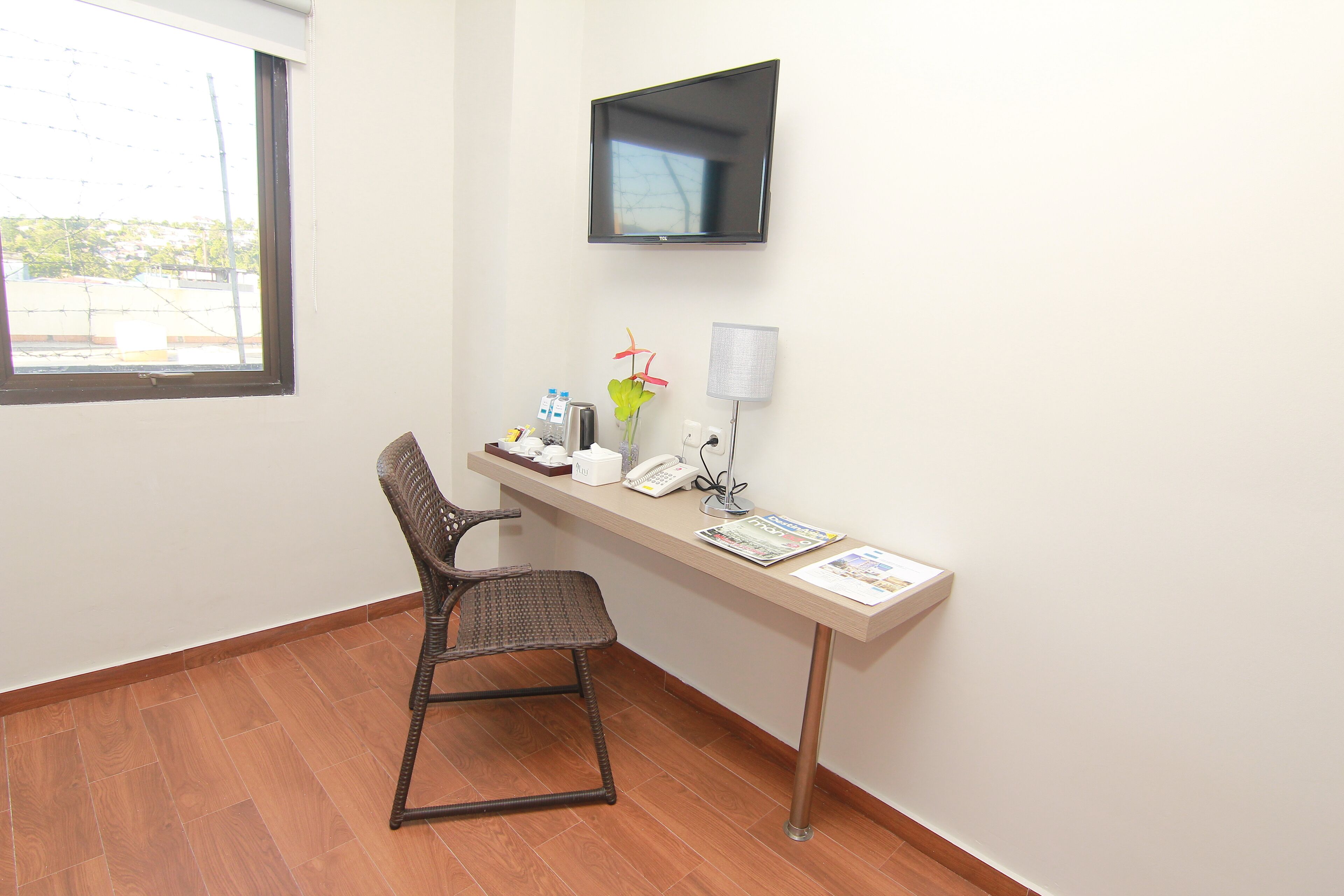 Una habitación con escritorio, silla, televisor, lámpara y ventana.