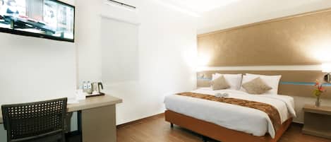 A hotel room with a bed, a desk, a chair, a TV, and a nightstand.