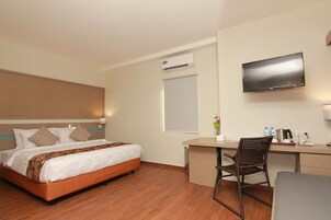 Habitación de hotel con cama, escritorio, silla, televisor, aire acondicionado y ventana.