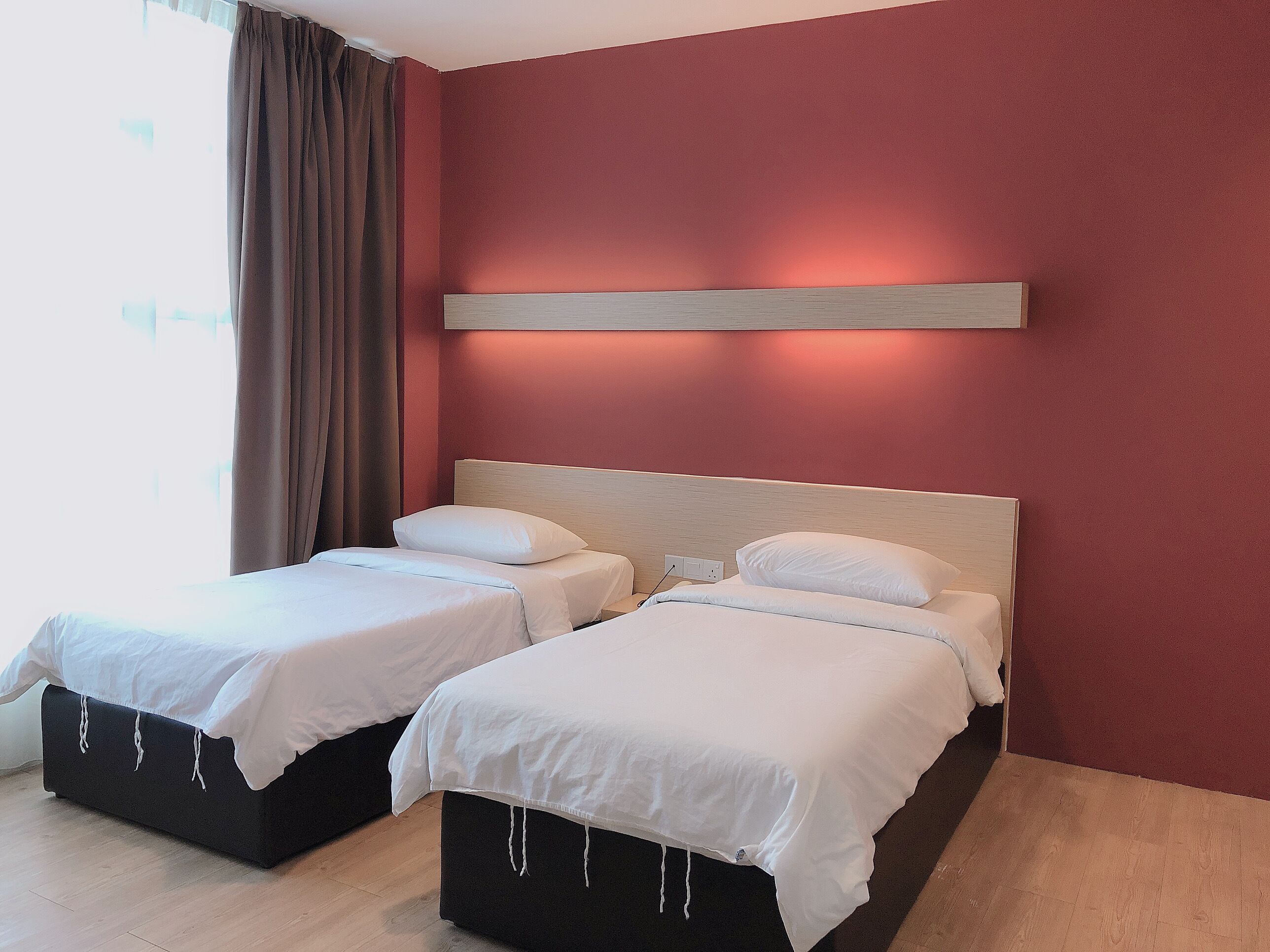 Habitación de hotel con dos camas, cabecero de madera y una pared de acento roja.
