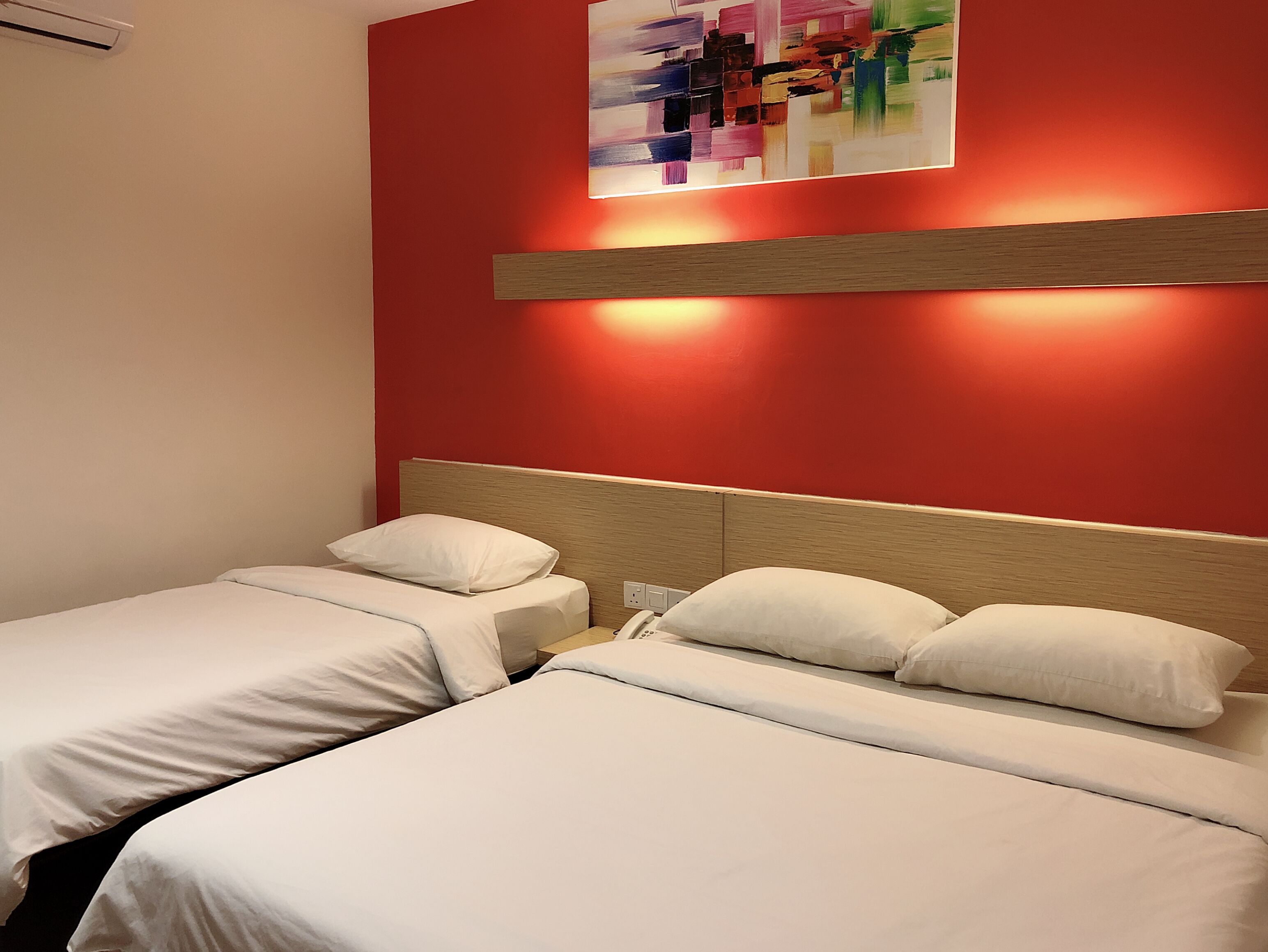 A hotel room with two beds, a red accent wall, and a painting above the beds.