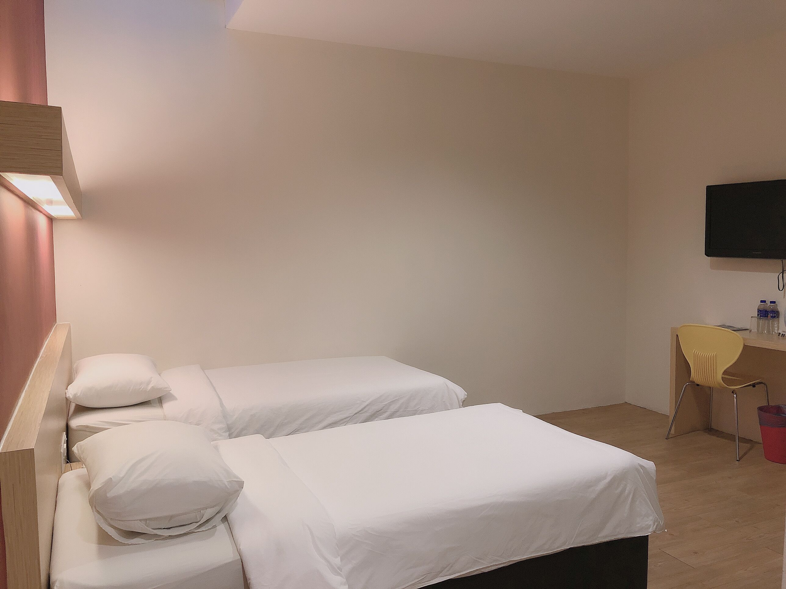 A hotel room with two single beds, a desk, a chair, and a TV mounted on the wall.