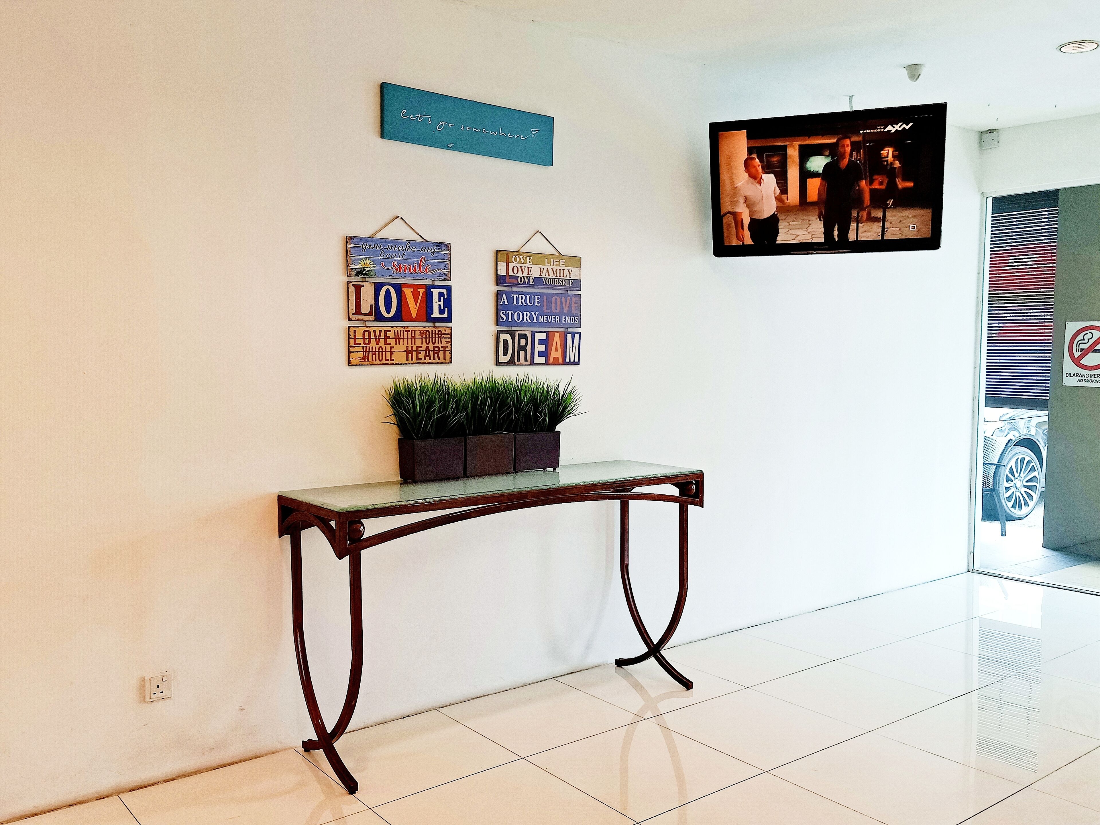 A reception area with a console table, potted plants, motivational wall art, and a mounted television.
