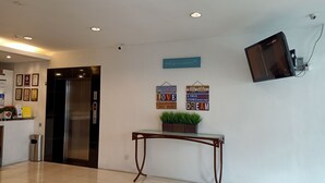 A lobby with a reception desk, a wall-mounted TV, a potted plant, and motivational signs. - Tras Mutiara Hotel Bentong (Bentong)