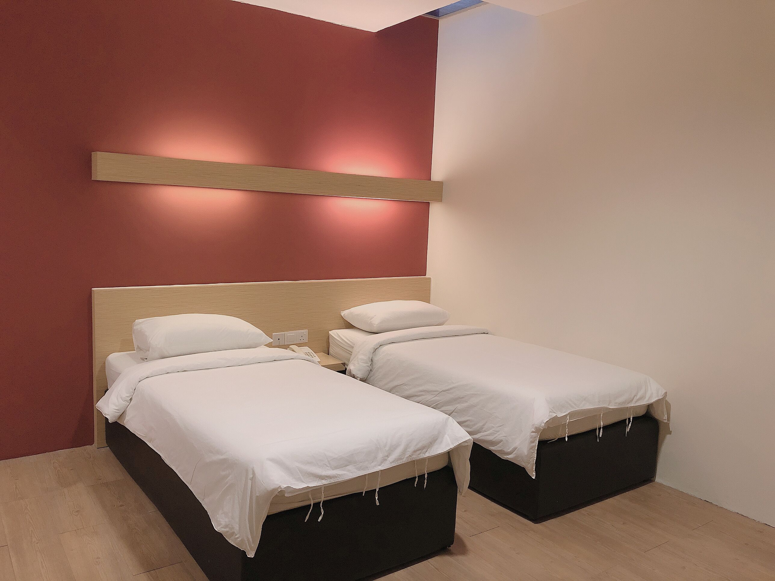 A hotel room with two beds, a wooden headboard, a red accent wall, and a bedside table with a phone.