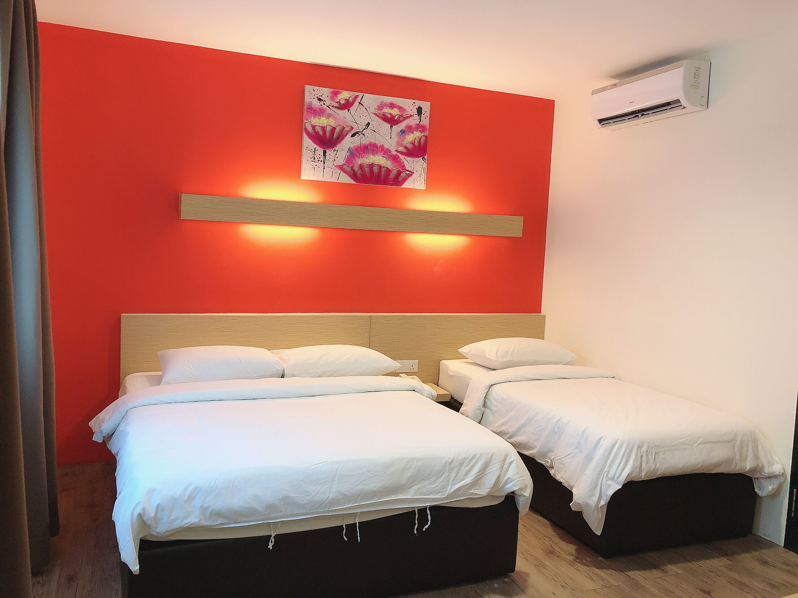A hotel room with two beds, a red accent wall, and an air conditioning unit.