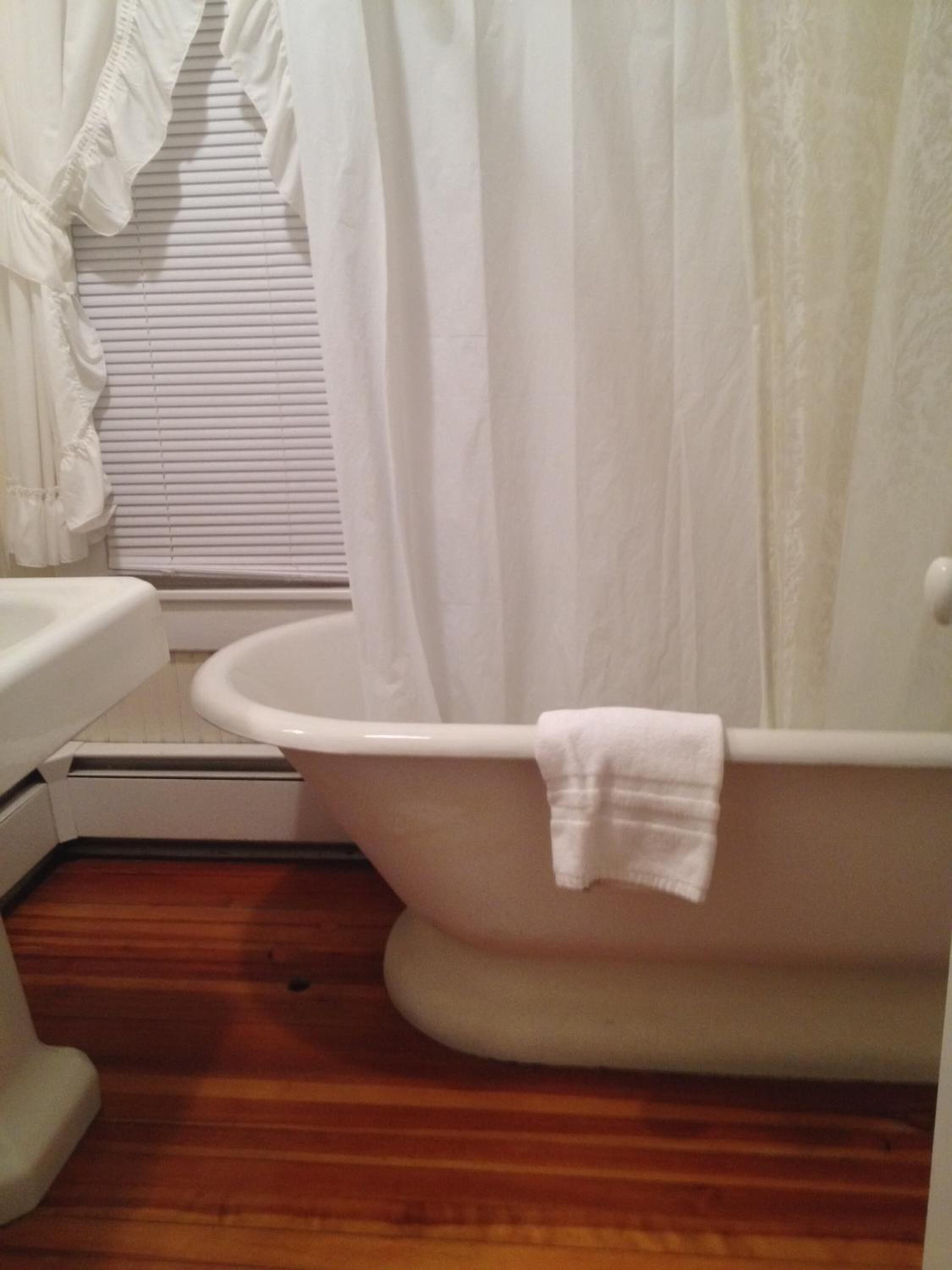 A bathroom with a white bathtub, a white sink, and a wooden floor.