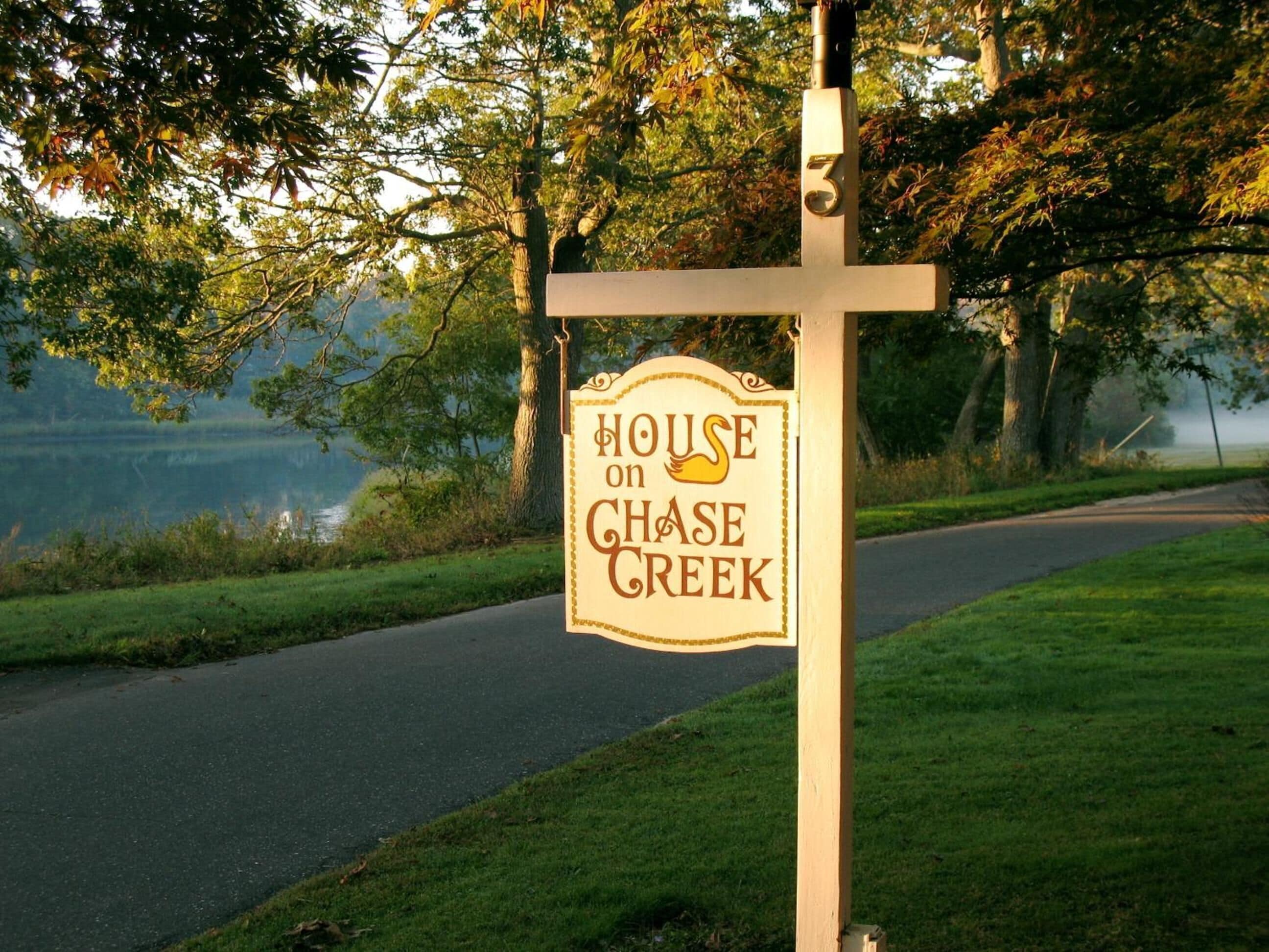 A sign for 'House on Chase Creek' with a view of a lake and trees in the background.