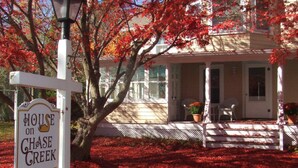 A house with a porch, a sign reading "House on Chase Creek," and a tree with red leaves. - House on Chase Creek (Shelter Island Heights)