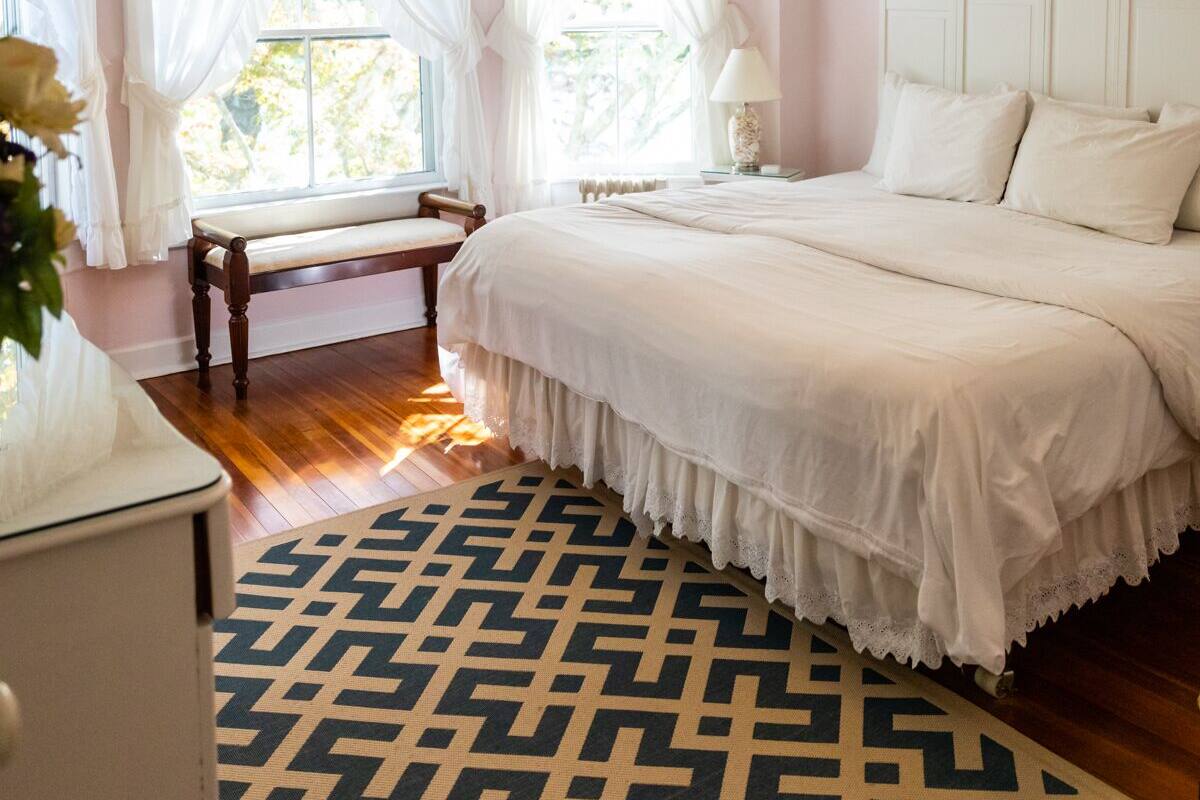 Un dormitorio con cama, mesita de noche, escritorio, silla, ventana con cortinas y ventilador de techo.