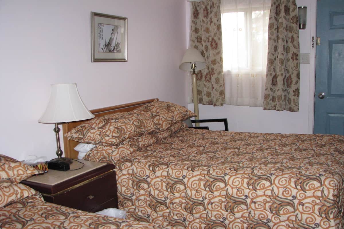 A neatly made bed with patterned bedding, a bedside lamp, a small wooden chest, and a framed picture on the wall.