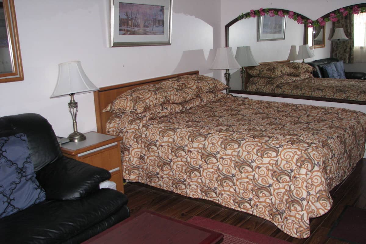 A bedroom with a bed, a chair, a nightstand, a lamp, and a mirror.