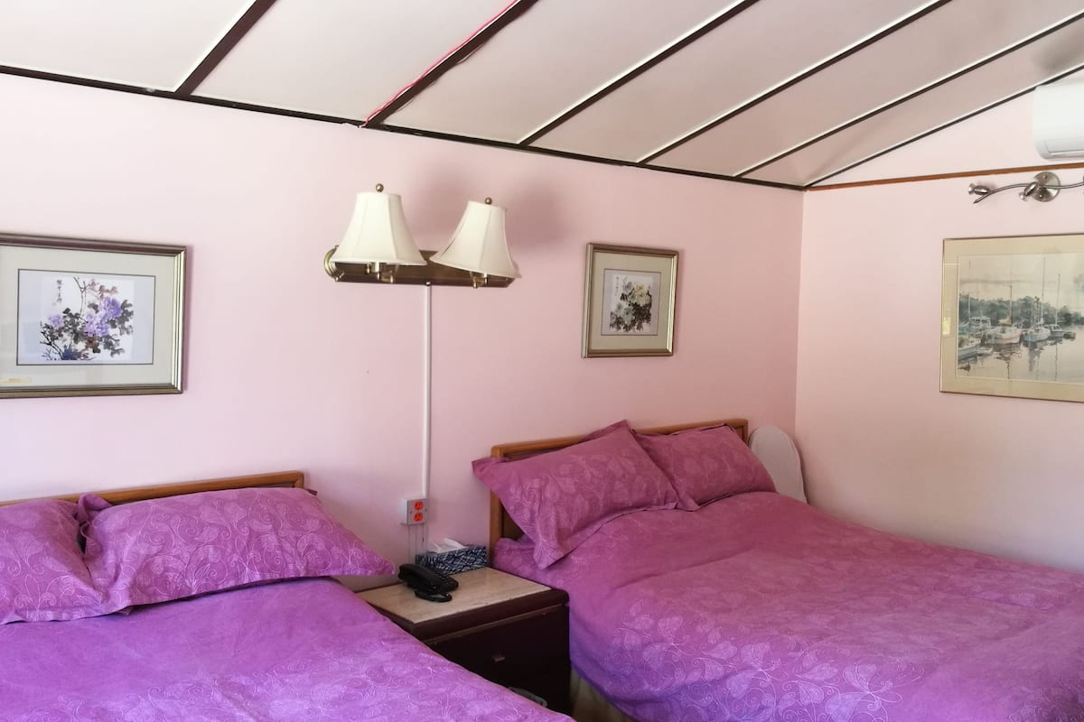 A bedroom with two beds, a bedside table with a lamp, and framed artwork on the walls.