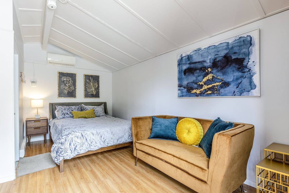 A bedroom with a bed, a sofa, a nightstand, and a wall-mounted artwork.