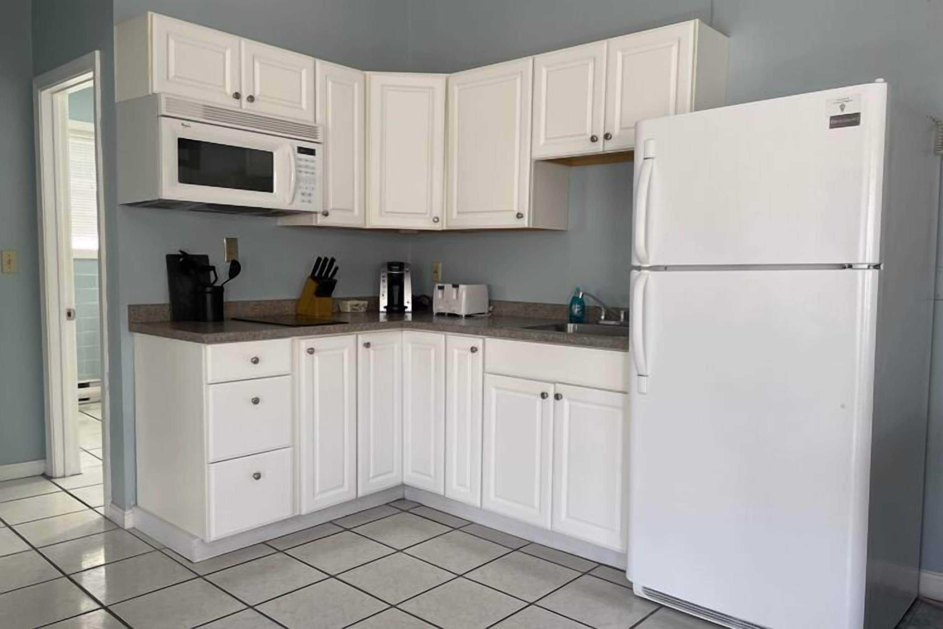 Una cocina con armarios blancos, microondas, tostadora y refrigerador.
