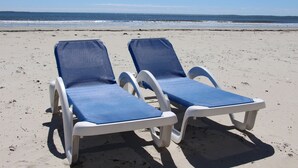 Dos sillas de playa con cojines azules sobre arena.