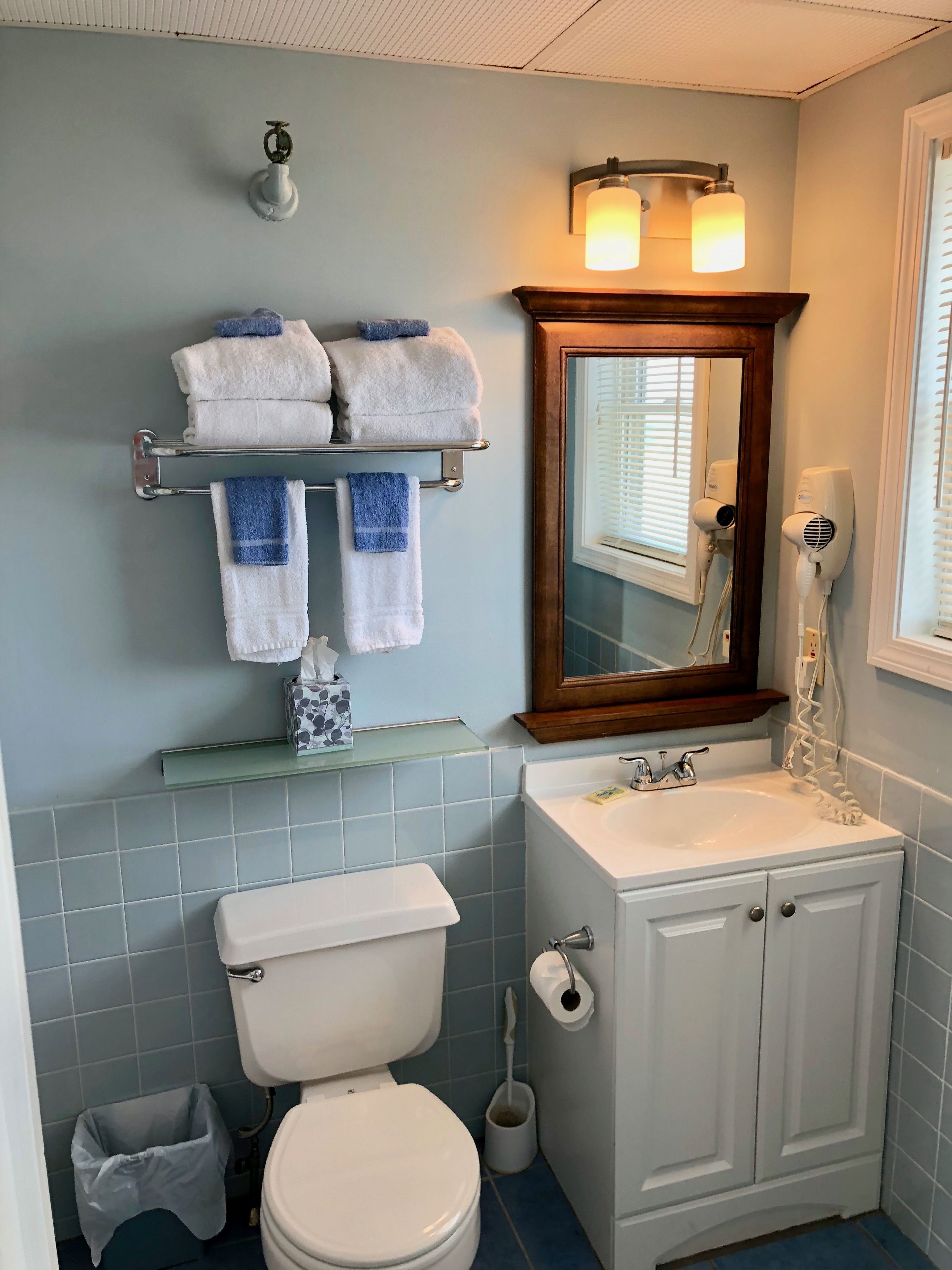 A bathroom with a toilet, sink, and mirror. There are towels on a rack and a hairdryer on the wall.