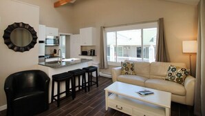 Una sala de estar moderna con un sofá, una mesa de centro y una zona de cocina con un ventanal grande.