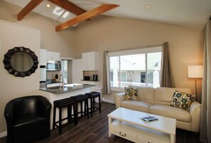 A modern living room with a sofa, coffee table, and a kitchen area with a large window. - Ocean Walk Hotel (Old Orchard Beach)