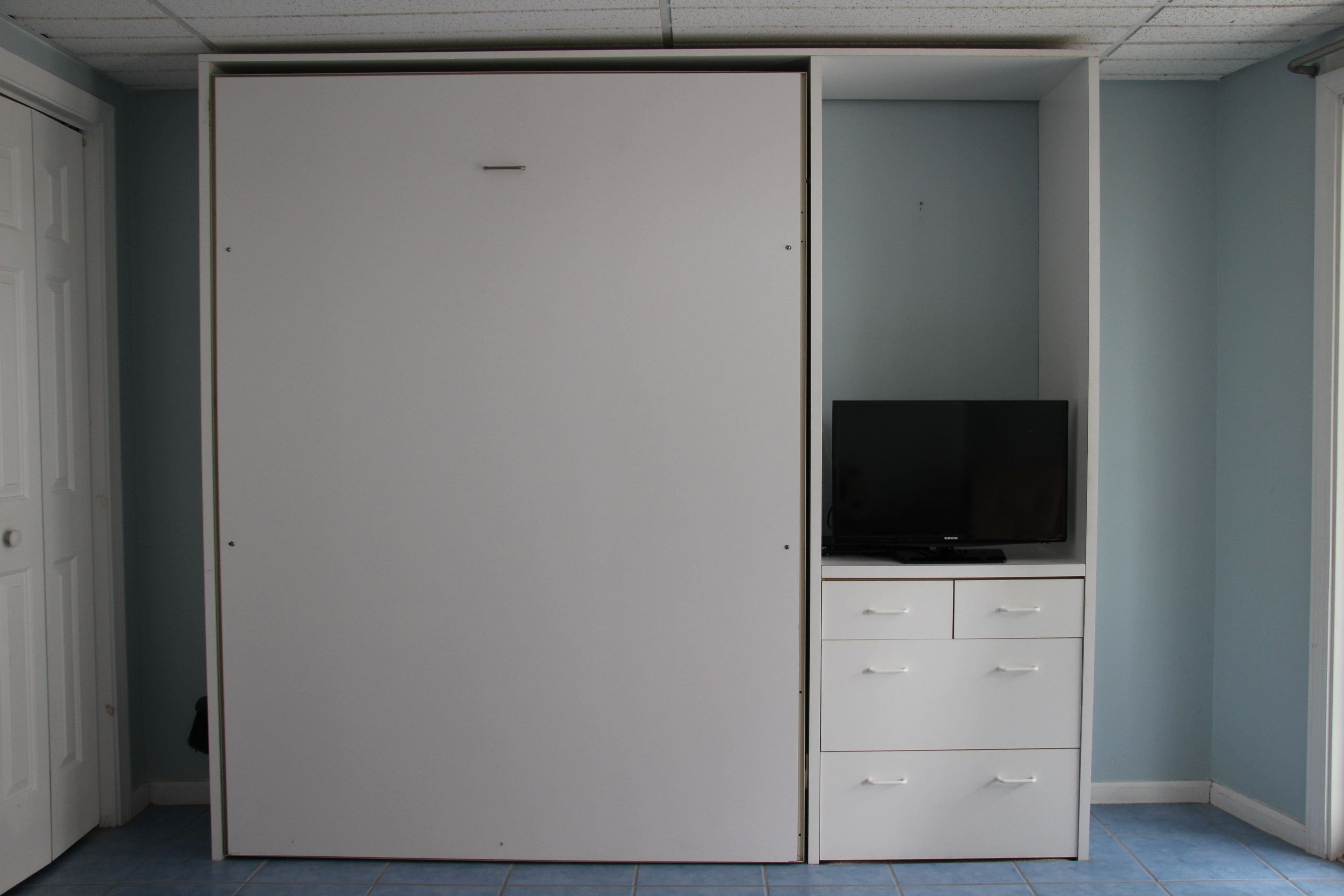 A room with a white wardrobe, a television on a stand, and a door.