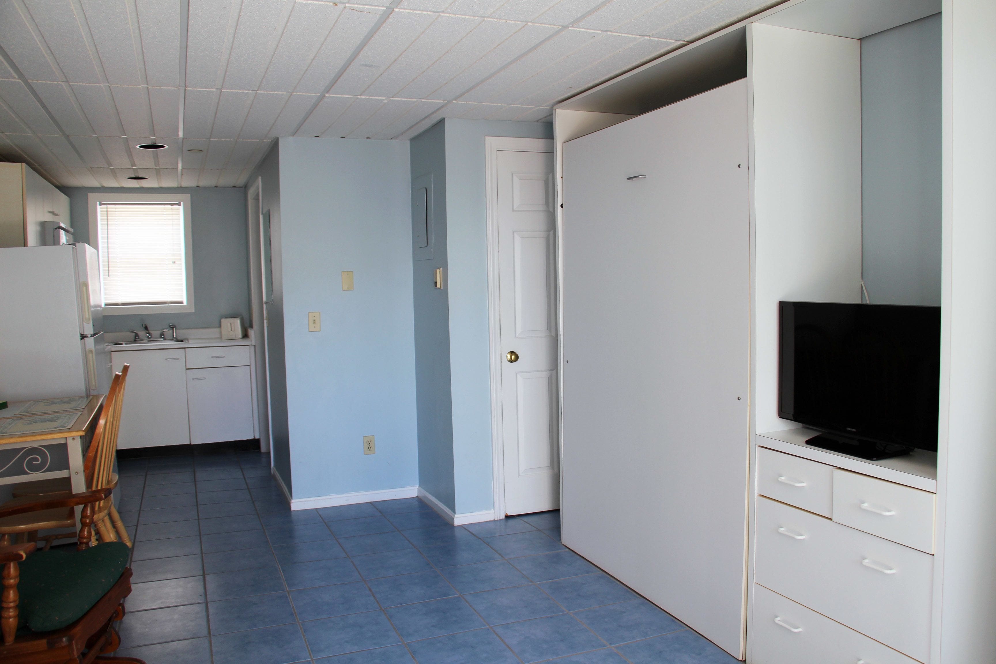 Una habitación con kitchenette, un comedor con mesa y sillas, y un televisor sobre un mueble.