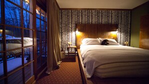 A hotel room with a large window, a bed with white linens, a nightstand, and a wall with vertical patterned wallpaper.