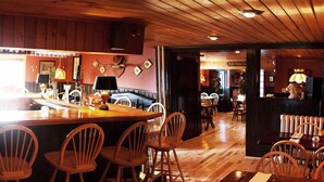 A restaurant interior with wooden flooring, wooden chairs, a bar area, and a dining section with tables and chairs.