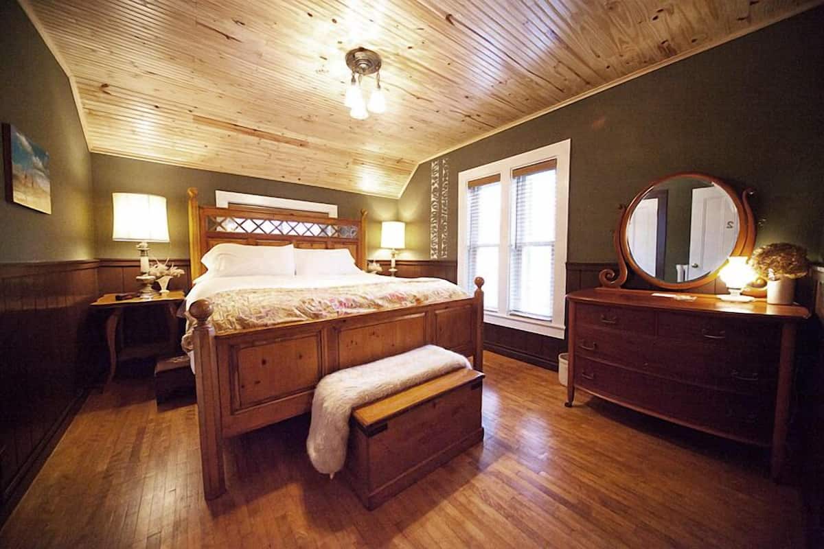 A wooden-paneled bedroom with a bed, bedside tables, a dresser, and a mirror.