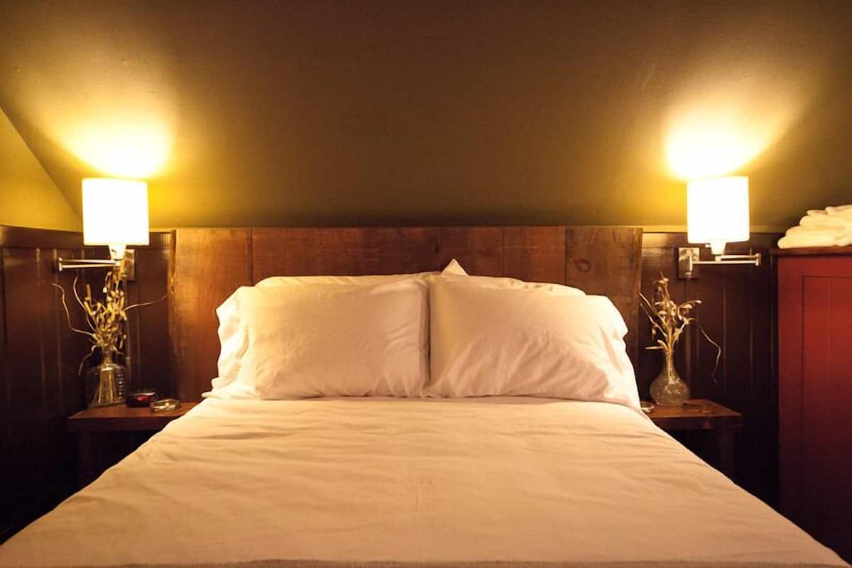 A neatly made bed with white linens, flanked by two bedside tables with lamps and vases.