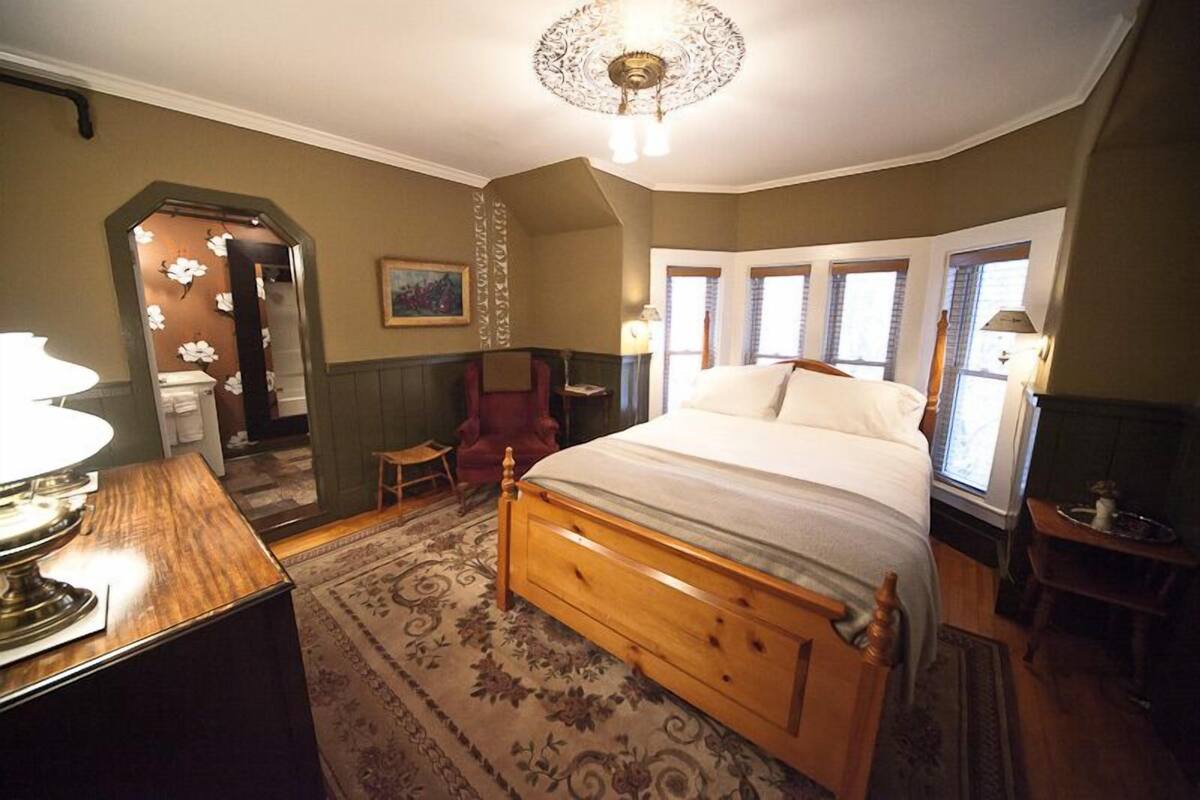 A bedroom with a wooden bed, a red chair, a small table, and a chandelier.