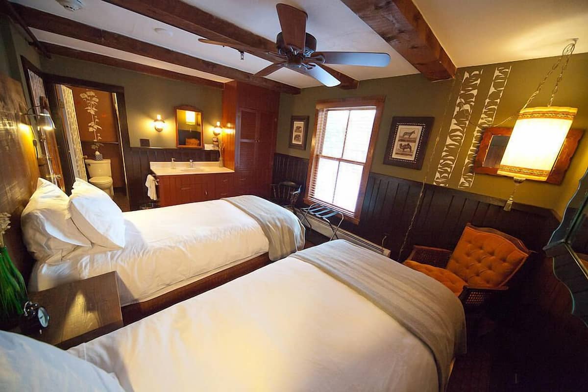 A hotel room with two beds, a bathroom, a ceiling fan, and a window.