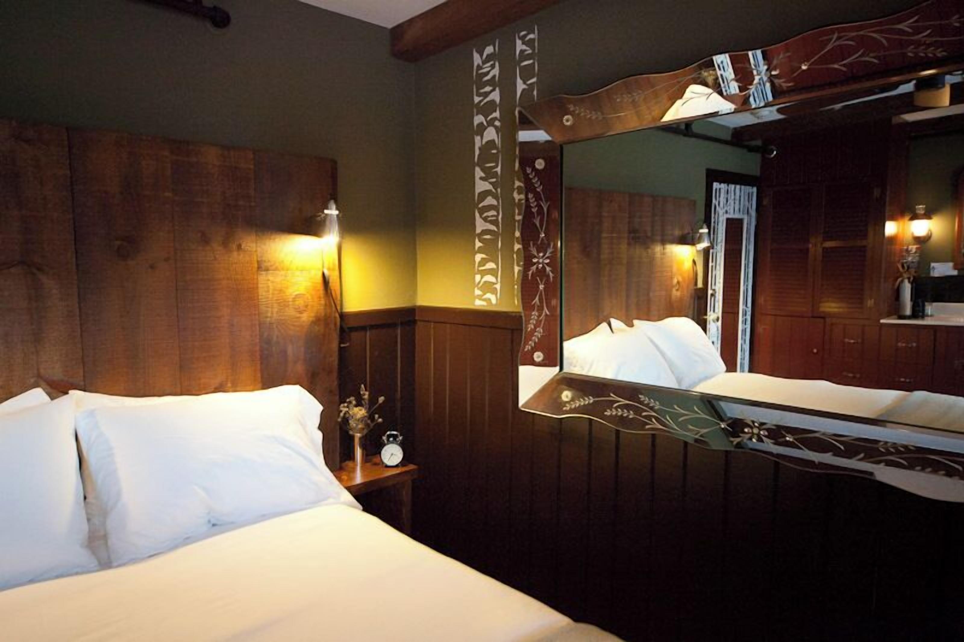 A hotel room with a wooden headboard, a large mirror, and a bedside table with a clock.