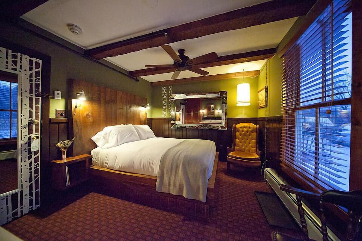 A bedroom with a bed, a chair, a ceiling fan, and a window with blinds.