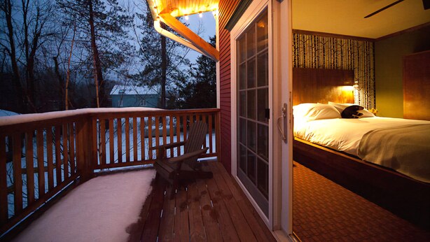 A bedroom with a large bed, a wooden deck, and a sliding glass door leading to a balcony.