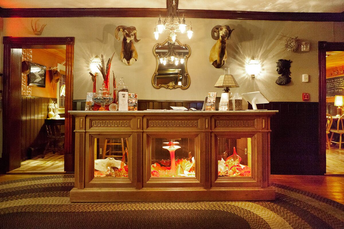 Un hall d’entrée avec un comptoir de réception en bois, un miroir et des têtes d’animaux décoratives accrochées au mur.