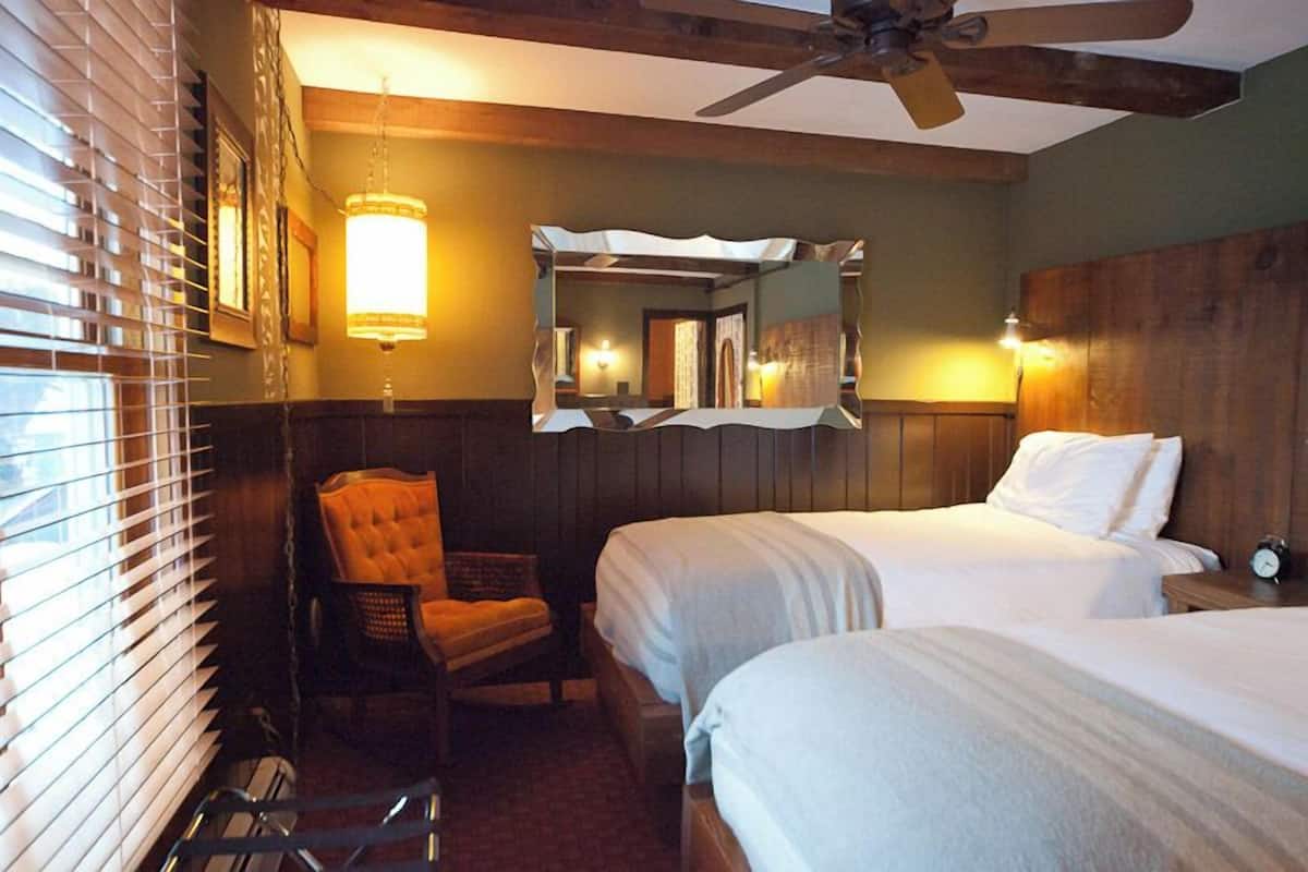 A hotel room with two beds, a chair, a ceiling fan, and a mirror.