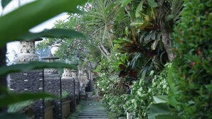 A stone pathway leading through a lush garden with various plants and a stone structure in the background. - Kubu Soca Villa (Ubud)