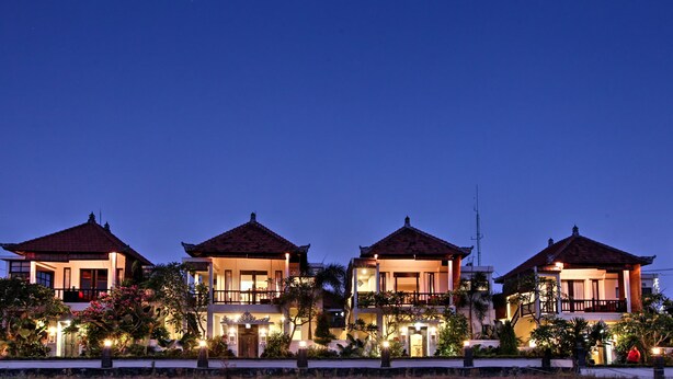 A row of four two-story buildings with traditional roofs, surrounded by well-maintained gardens and illuminated by exterior lighting. - Kubu Soca Villa (Ubud)