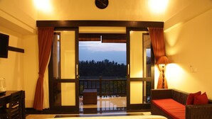 A hotel room with a large bed, a sofa, a desk, and a balcony with a view of the trees. - Kubu Soca Villa (Ubud)