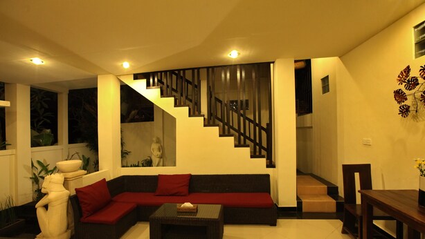 A modern living room with a sectional sofa, a coffee table, a staircase with a railing, and a wall-mounted sculpture. - Kubu Soca Villa (Ubud)